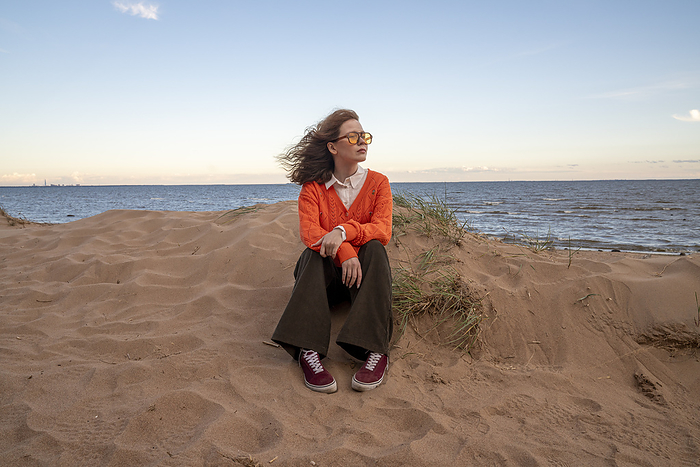 Contemplative young woman sitting on sand at beach