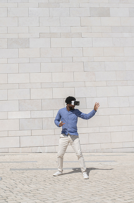 Young man wearing virtual reality simulator gesturing in front of wall