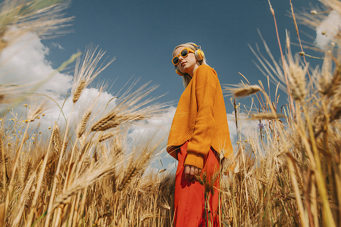 Woman wearing bluetooth headphones standing in wheat field
