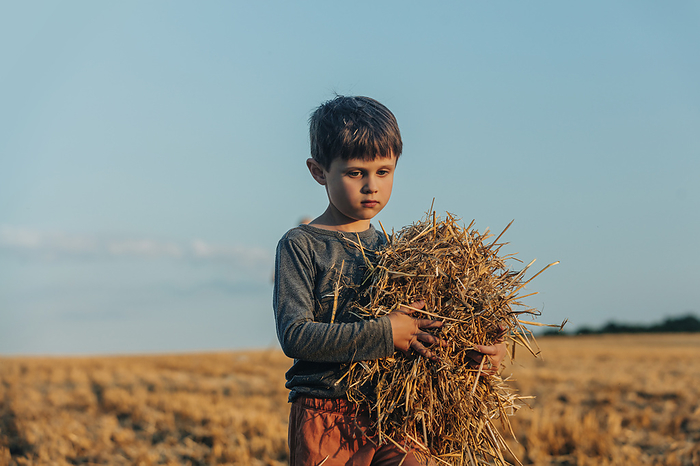 Contemplative boy standing with hay in wheat field
