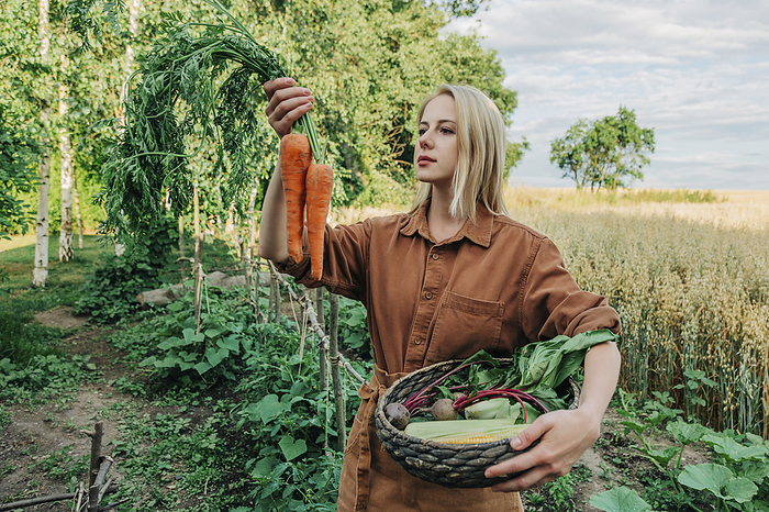 Blond woman examining carrots standing in garden