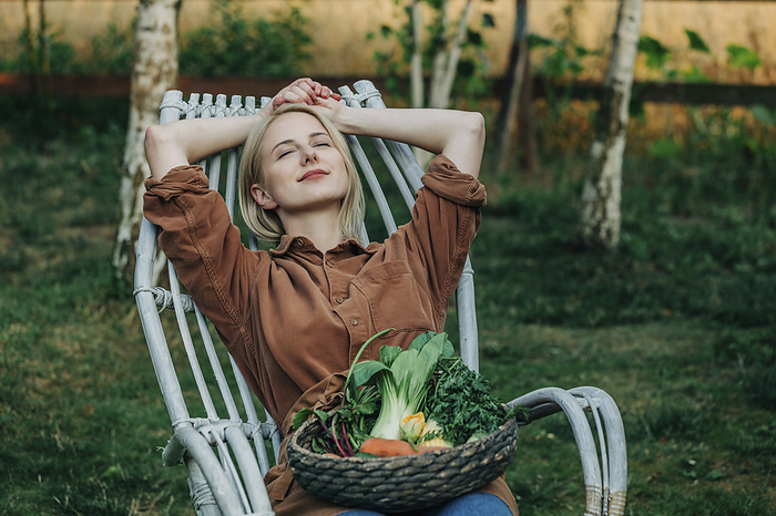 Smiling woman leaning on chair with vegetable basket in garden