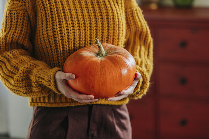 Woman wearing sweater and holding pumpkin at home