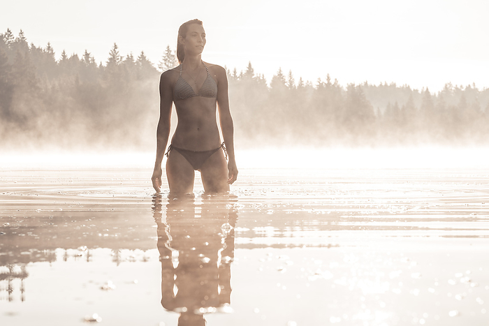 Woman wearing bikini bathing in a lake at morning mist