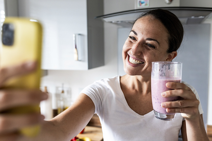 Happy woman clicking selfie with milkshake at home