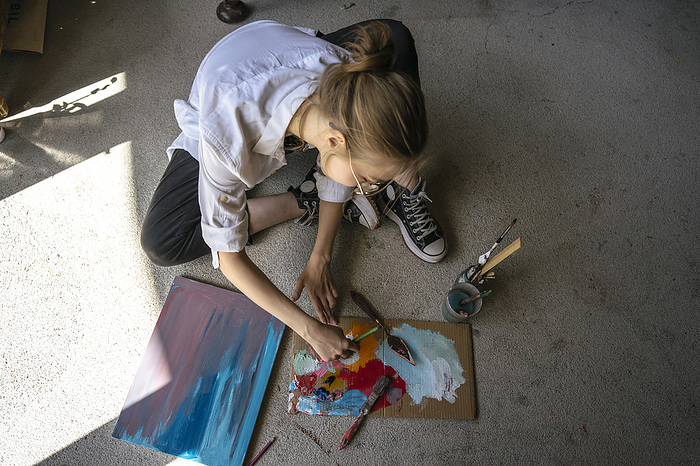 Artist sitting on carpet and painting at workshop