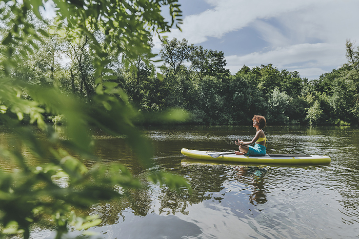 Young woman sitting and meditating on paddleboard in lake