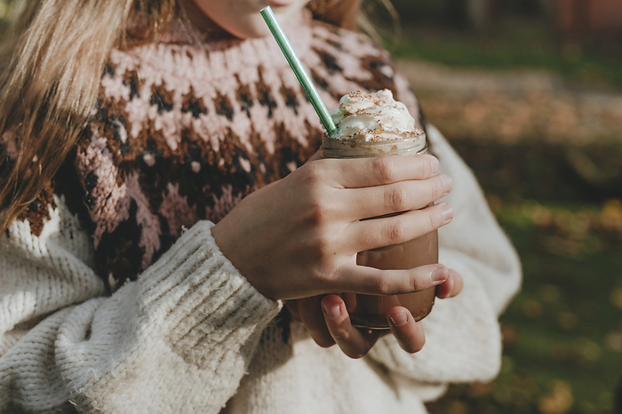 Girl wearing sweater holding jar of milkshake