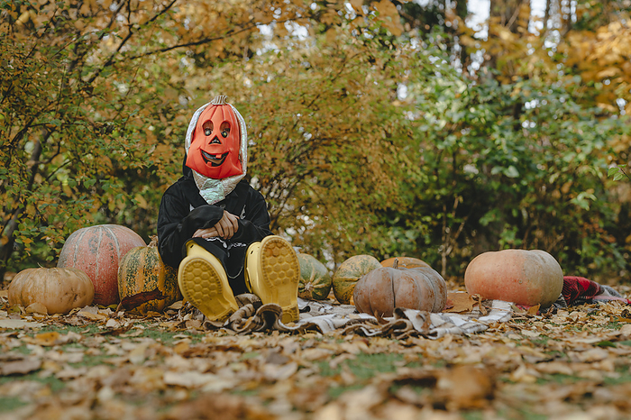 Playful girl in halloween costume sitting amidst pumpkins in garden