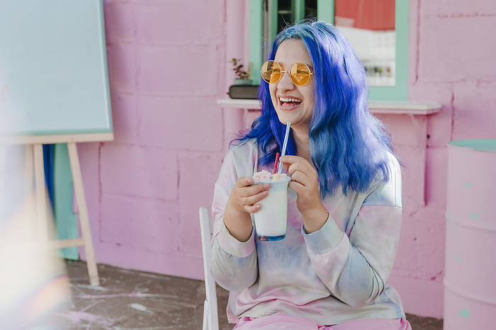 Happy woman with dyed blue hair holding drink at cafe