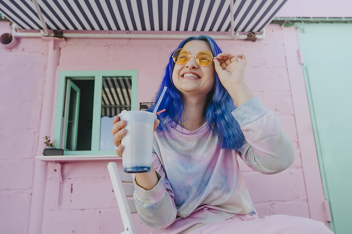 Happy woman with dyed blue hair holding milkshake at cafe
