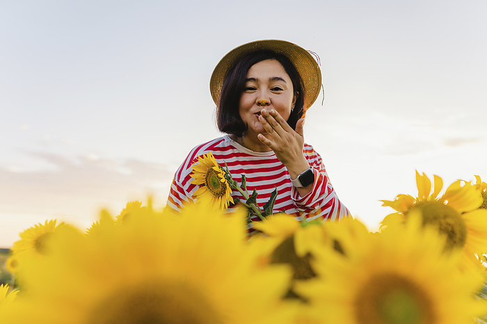 Woman with hat blowing kiss in sunflower field