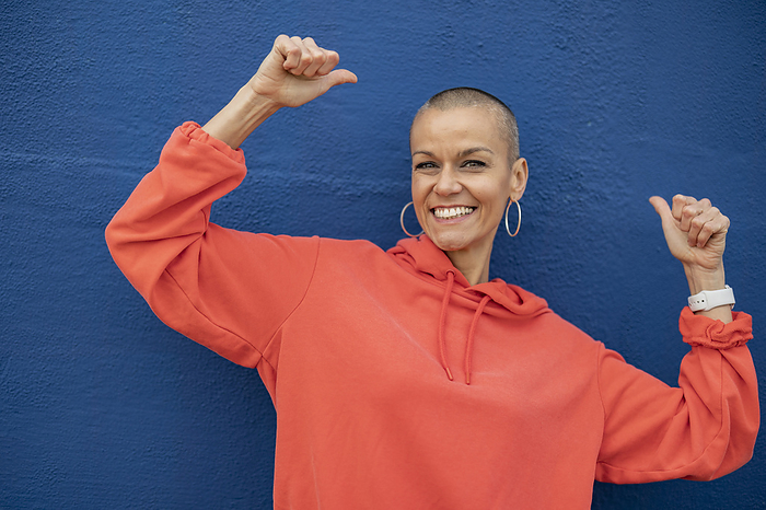 Happy woman with shaved head dancing in front of blue wall