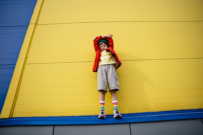 Boy with arms crossed on head standing in front of yellow wall