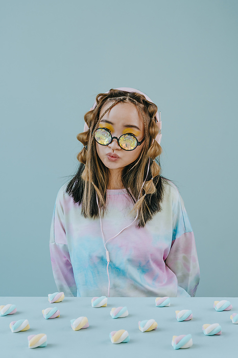 Woman with kaleidoscope glasses puckering by marshmallows on table against blue background