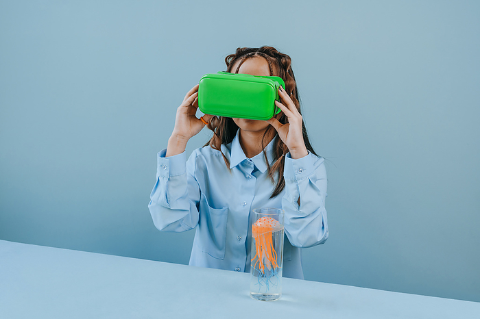 Woman watching VR glasses by jellyfish in glass on table against blue background