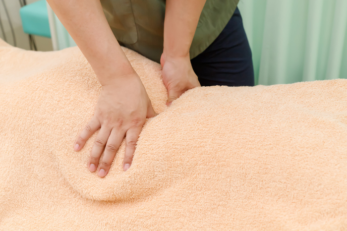 Image of an osteopath or massage therapist examining or performing a procedure with a patient with back symptoms and back pain. Close-up of a hand
