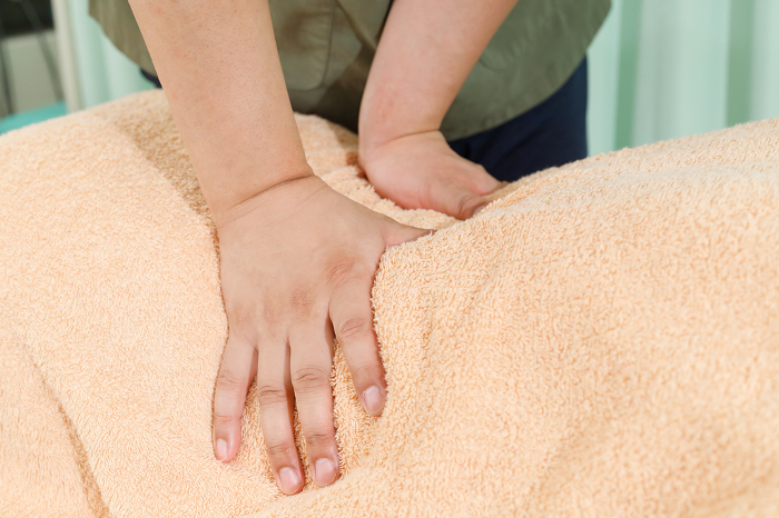 Image of an osteopath or massage therapist examining or performing a procedure with a patient with back symptoms and back pain. Close-up of a hand