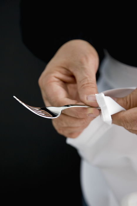 Close up of a waiter hands polishing a silver fork with a white napkin, by Ableimages