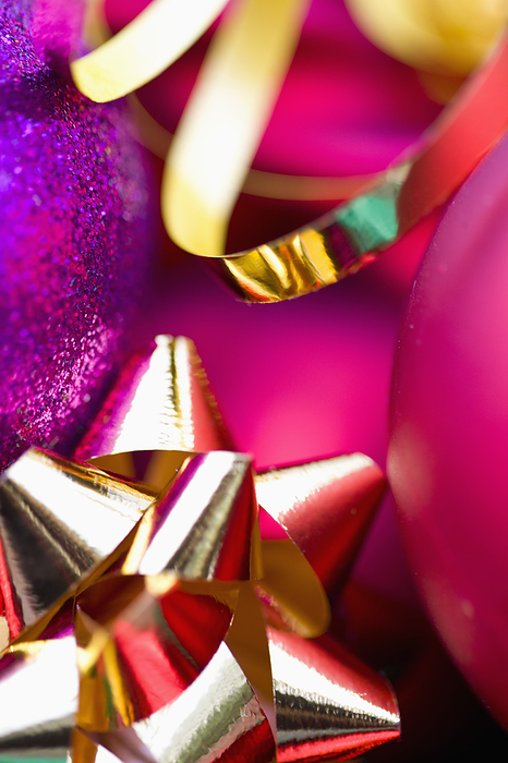 Extreme close up of red and purple Christmas baubles and a gold bow and ribbon, by Ableimages