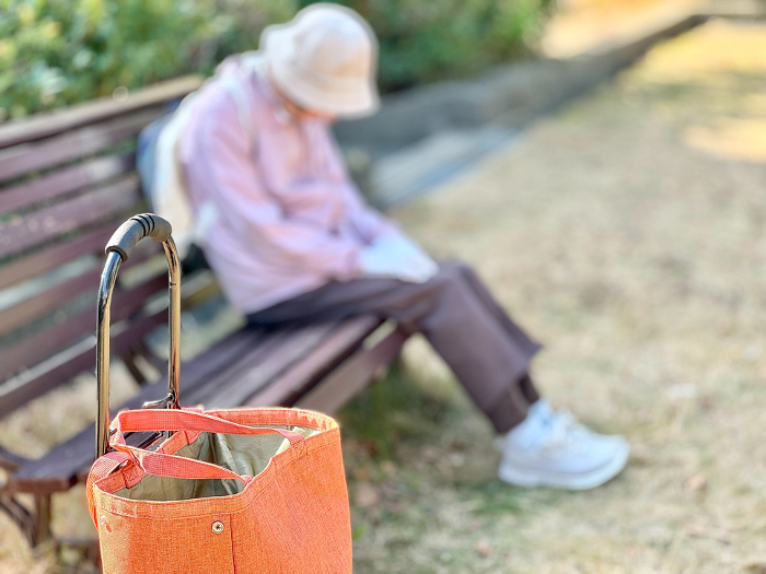 Elderly woman sitting on bench and nodding off with shopping cart