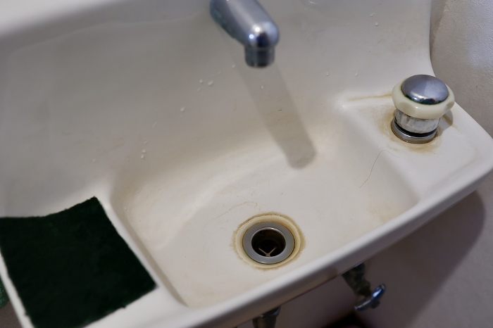 Water stains around the drain in the hand washing basin of the toilet.