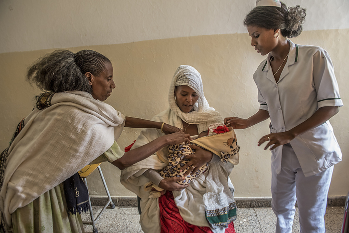 Newborn baby Mother with her newborn baby at Lemlem Karl Hospital in Maichew, in the Tigray region of Ethiopia. Both her own mother, left, and a nurse, right, advise her on caring for the baby., by KAREN KASMAUSKI SCIENCE PHOTO LIBRARY