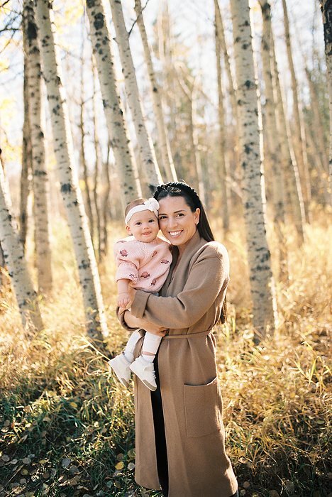 Mom holding smiling baby girl in yellow fall leaves and autumn forest, by Cavan Images / Samantha Joy Shantz Photography