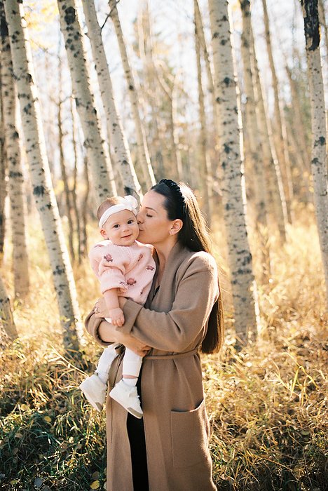 Mom kissing smiling baby girl in front of yellow fall trees, by Cavan Images / Samantha Joy Shantz Photography