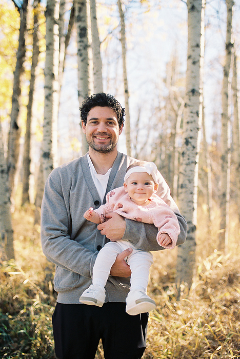 Young dad holding baby girl in front of fall leaves and forest, by Cavan Images / Samantha Joy Shantz Photography
