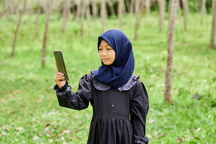 Portrait of asian muslim girl taking selfies on rubber forest, by Cavan Images / Anucha Muphasa