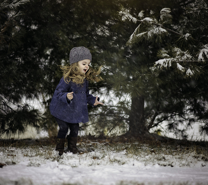 Little girl with long curls jumping and playing in snow, by Cavan Images / Joy Faith