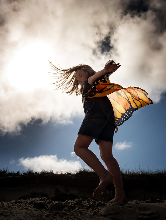 Girl spinning with butterfly wings outdoors, by Cavan Images / Joy Faith