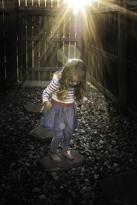 Little girl hopping on stones in back yard, by Cavan Images / Joy Faith