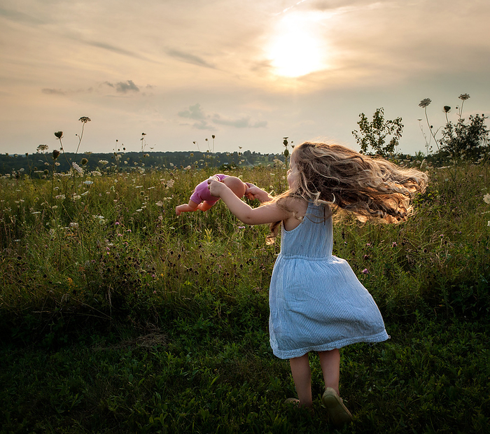 Little girl with long blonde curls spinning in dress outdoors, by Cavan Images / Joy Faith