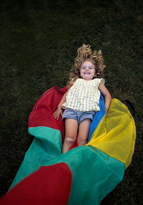 Beautiful toddler playing in yard on colorful textile, by Cavan Images / Joy Faith