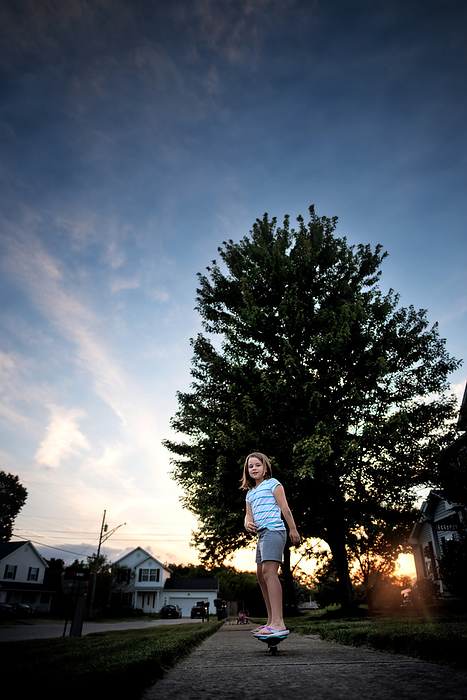 Happy little girl riding skateboard outside in summer, by Cavan Images / Joy Faith