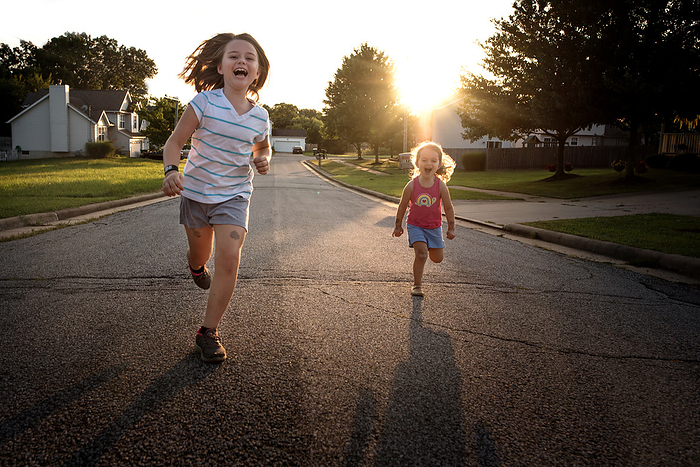 Happy sisters running and playing at sunset, by Cavan Images / Joy Faith