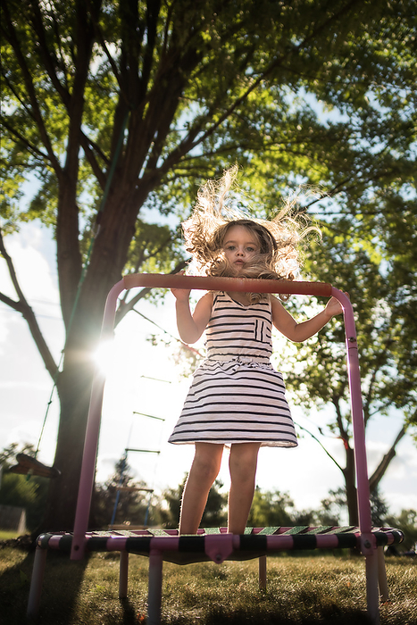 Beautiful little girl jumping on trampoline in back yard, by Cavan Images / Joy Faith