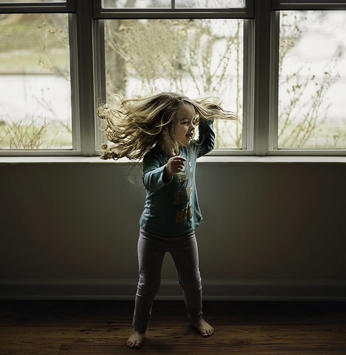 Happy little girl with long curls dancing in living room, by Cavan Images / Joy Faith