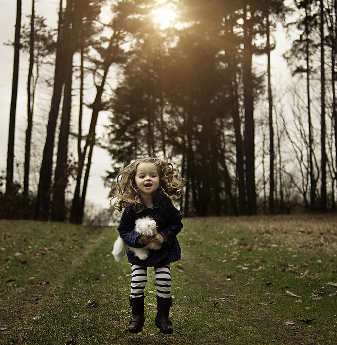 Happy little girl jumping with stuffed toy in field, by Cavan Images / Joy Faith