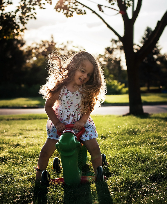 Happy little girl with long curls playing on outdoor toy, by Cavan Images / Joy Faith