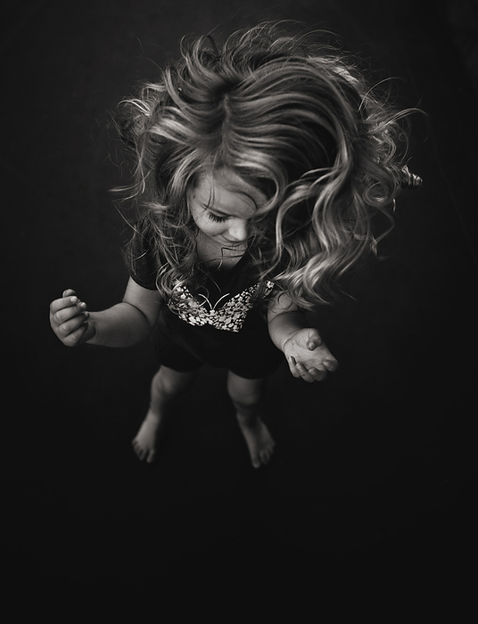 Little girl with long curls jumping on trampoline, by Cavan Images / Joy Faith