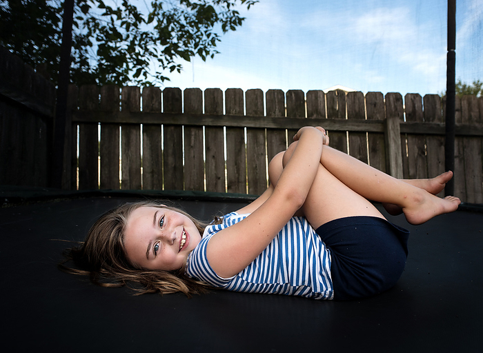Beautiful little girl smiling while laying outside in summer, by Cavan Images / Joy Faith