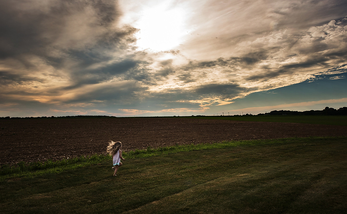 Little girl hair blowing while walking through field, by Cavan Images / Joy Faith