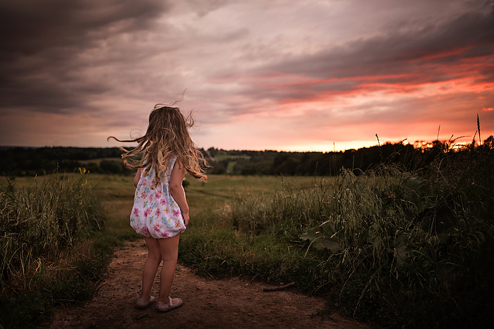 Toddler with long curls watching beautiful sunset, by Cavan Images / Joy Faith