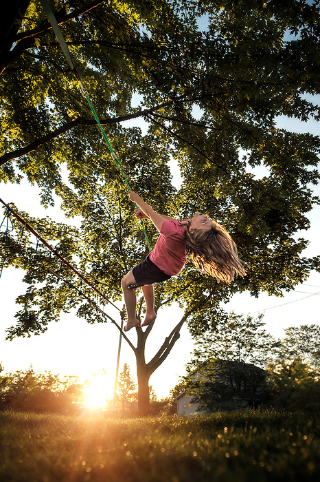 Young girl spinning on tree swing in summer, by Cavan Images / Joy Faith