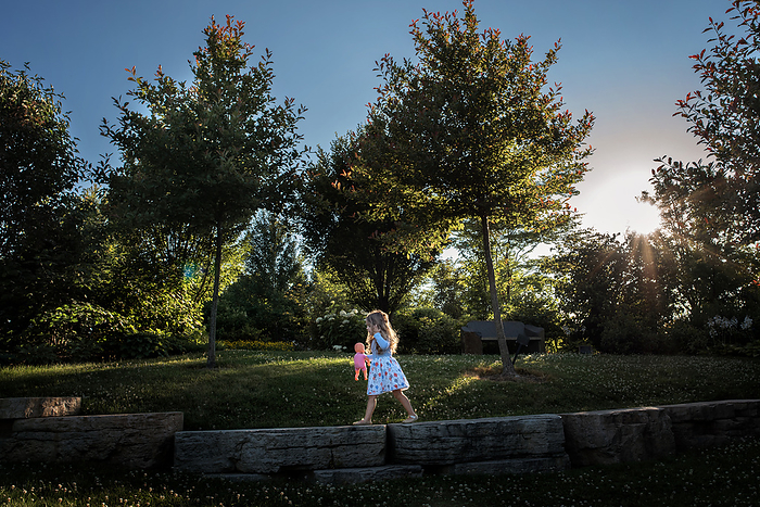 Cute little girl walking outdoors holding baby doll, by Cavan Images / Joy Faith