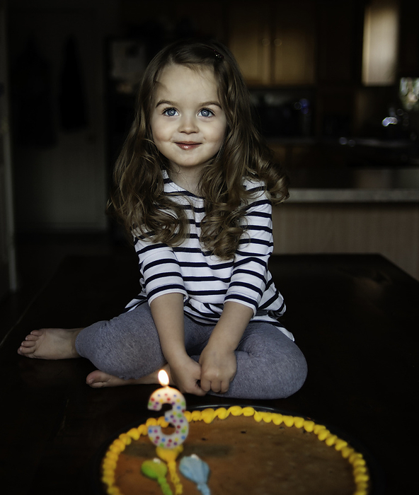 Happy little girl smiling with birthday cake, by Cavan Images / Joy Faith