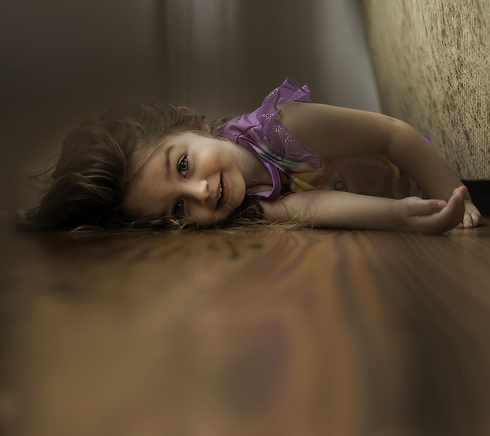 Beautiful little girl laying on floor in pajamas smiling, by Cavan Images / Joy Faith